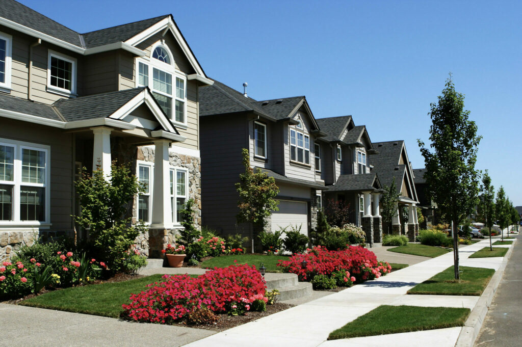 Bright sunny day on a beautiful subdivision street with large homes, landscaping, red and pink flowers