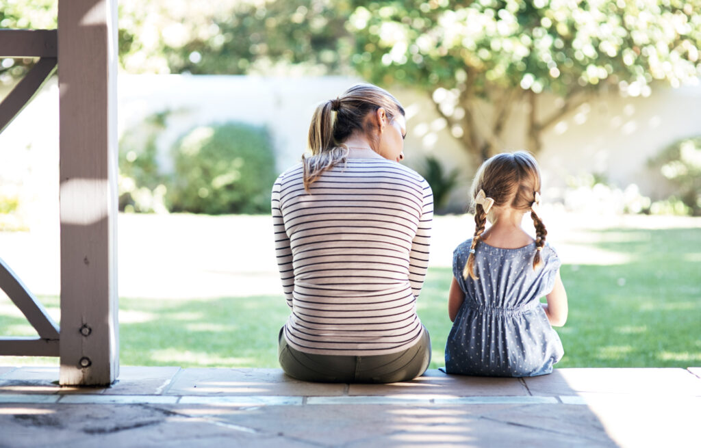 Mother and her young daughter sitting on the porch steps on a sunny day