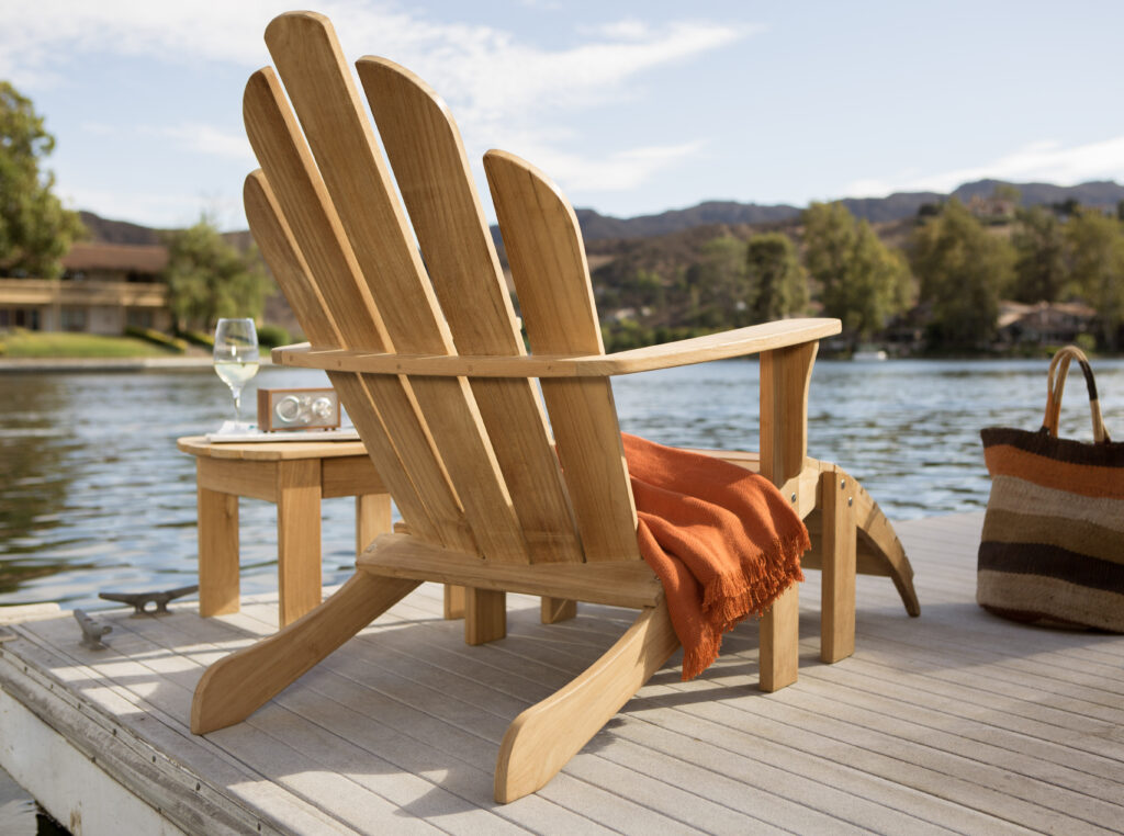 Natural wood muskoka chair on dock draped with orange blanket, small table beside chair with wine glass and portable speaker