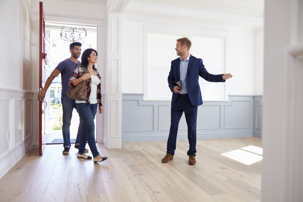 Realtor in a blue suit shows a young couple a property, couple entering through front door