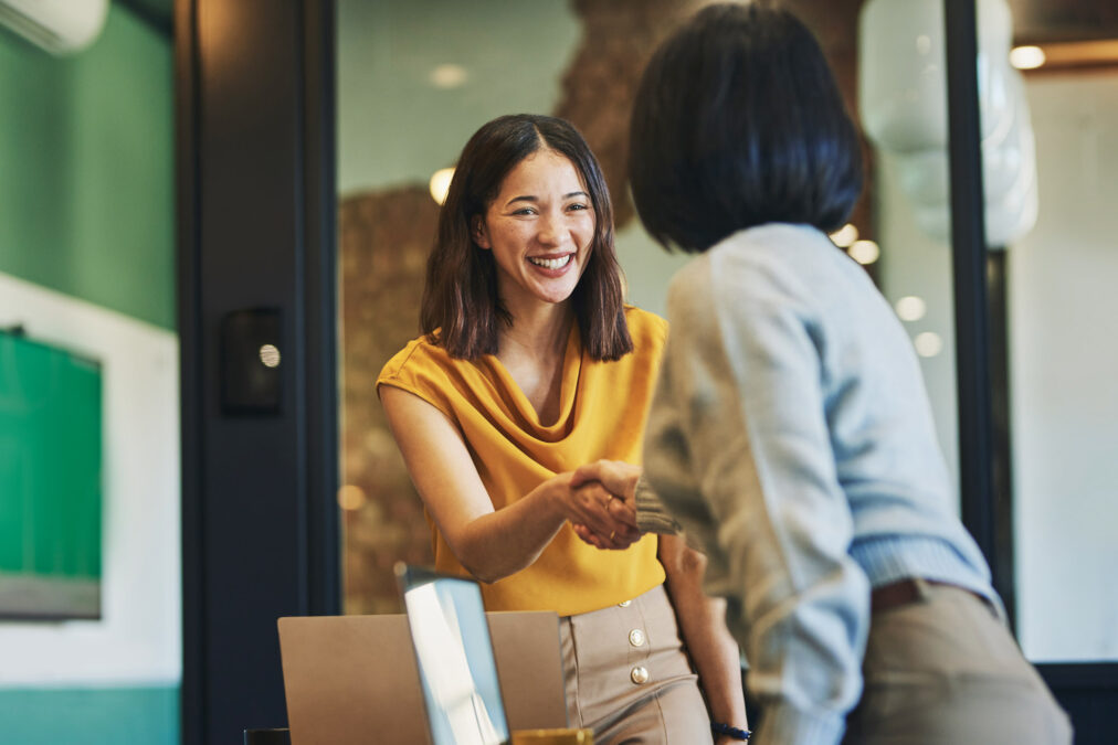 A young woman shakes the hand of another woman in professional business attire