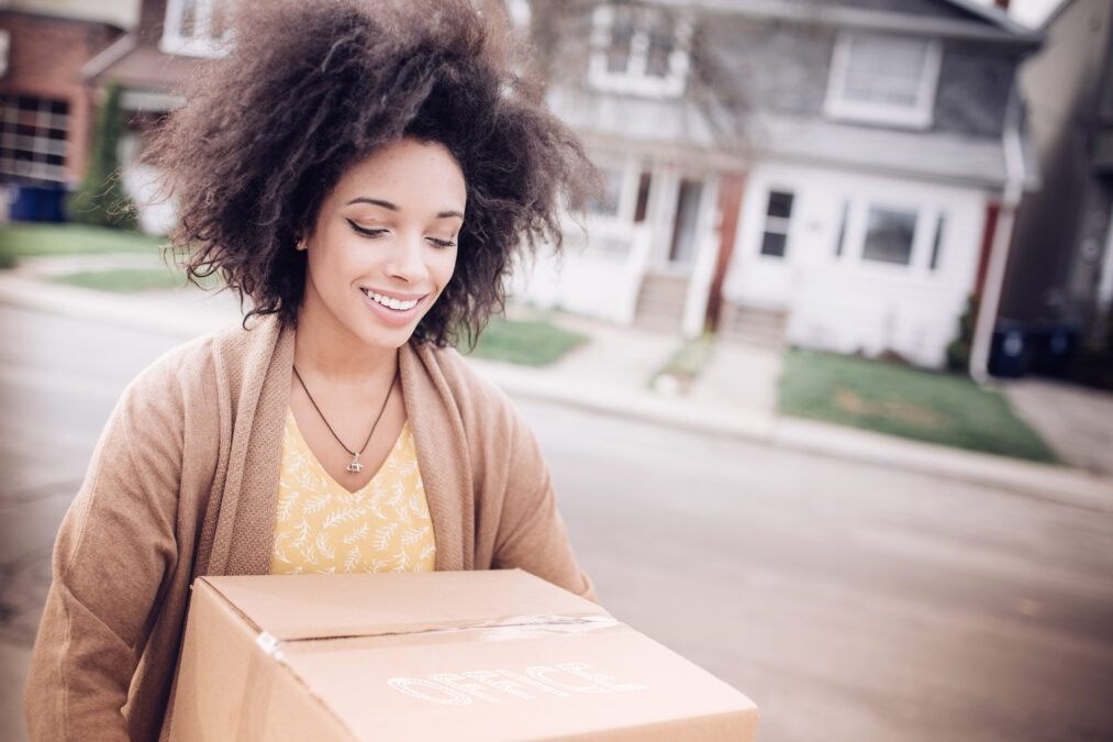 Happy, young woman carrying a moving box to her new home