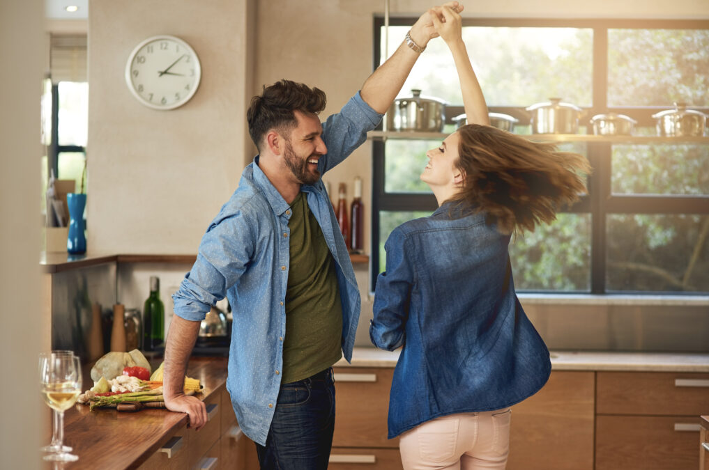 Young, happy couple dancing in the kitchen; warm sunlight pouring in through the window