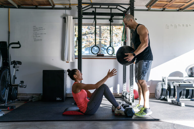 A couple does a workout together in the gym they have set up in the garage of their home.