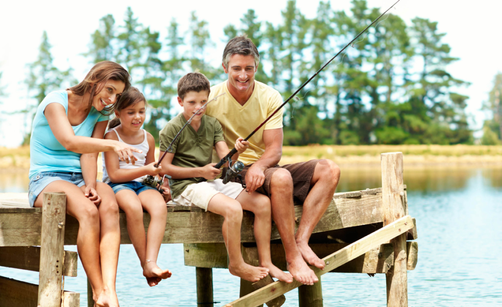 Mother and father sitting on a dock with their daughter and son who are fishing, smiling