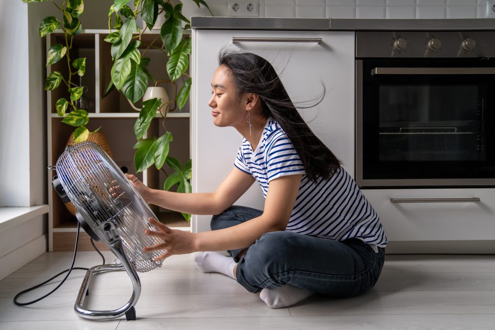 A young woman sitting in front of a fan on a kitchen floor