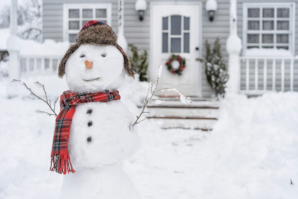 Snowman with plaid hat and scarf outside a home in winter