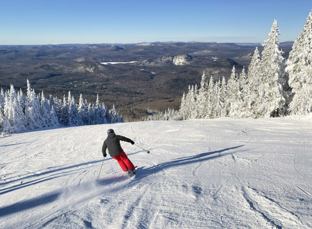Skier in red snow pants atop a large mountain, heading downhill