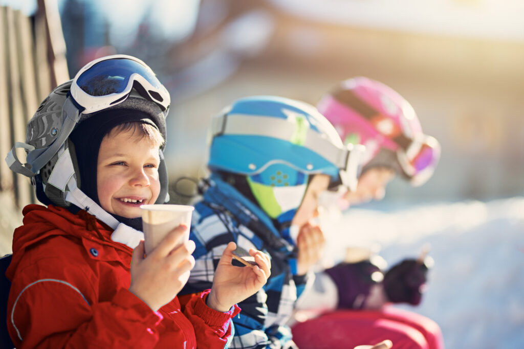 young children at the base of a ski hill drinking hot chocolate