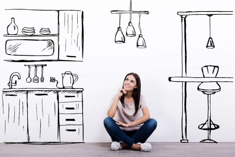 Young woman sitting on the floor of a room imagining what her new kitchen will look like