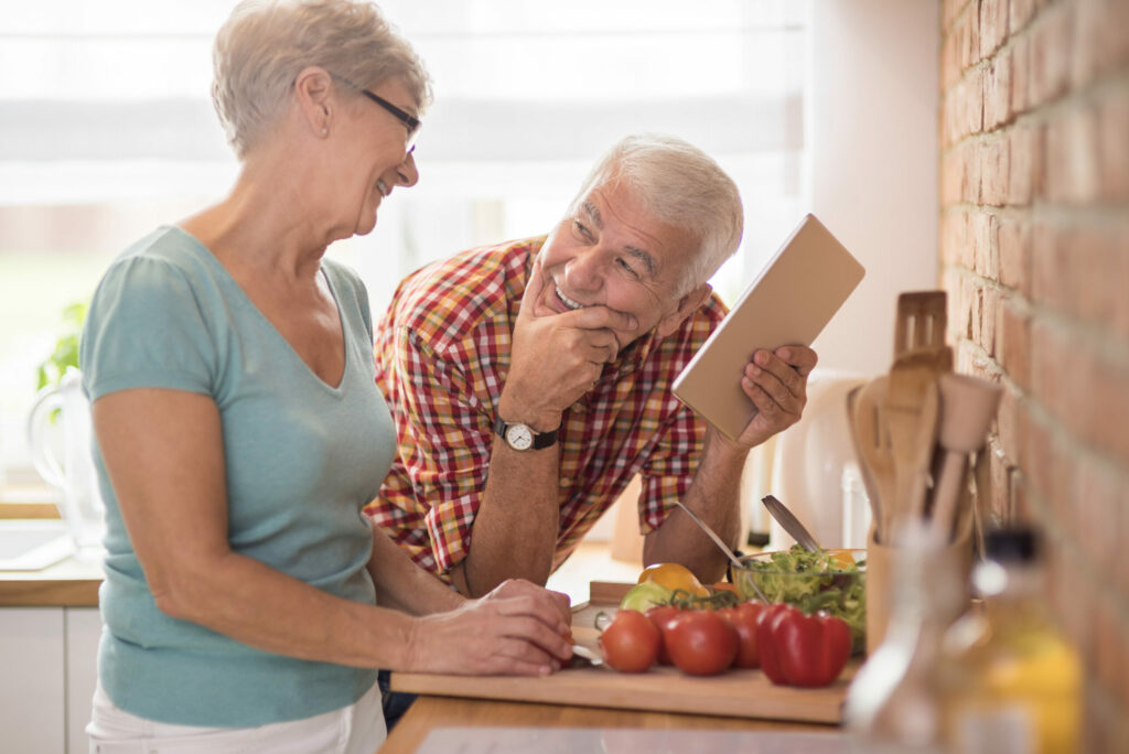 Elderly couple laughing and smiling in their kitchen while preparing a meal