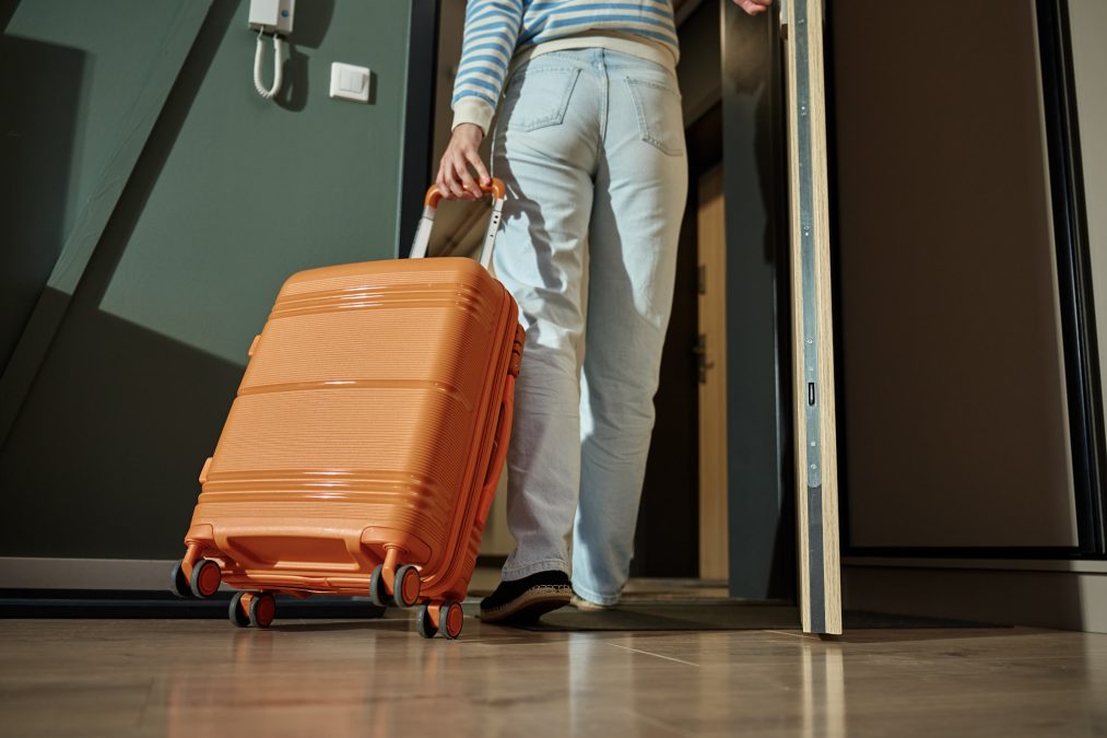 Woman exits from apartment with orange suitcase