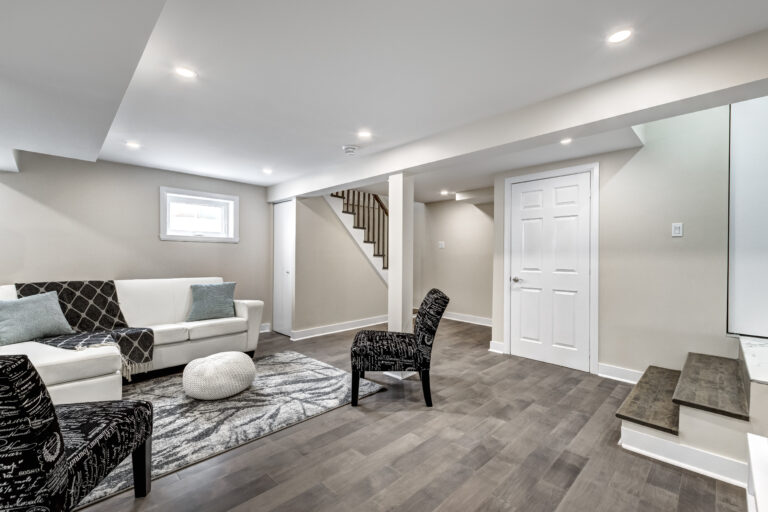 Modern renovated basement with grey hardwood floors, white couch and black accent chairs