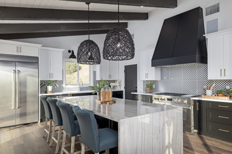 Interior of dark, modern luxury kitchen with marble waterfall island, blue bar stools, and black woven pendant lights