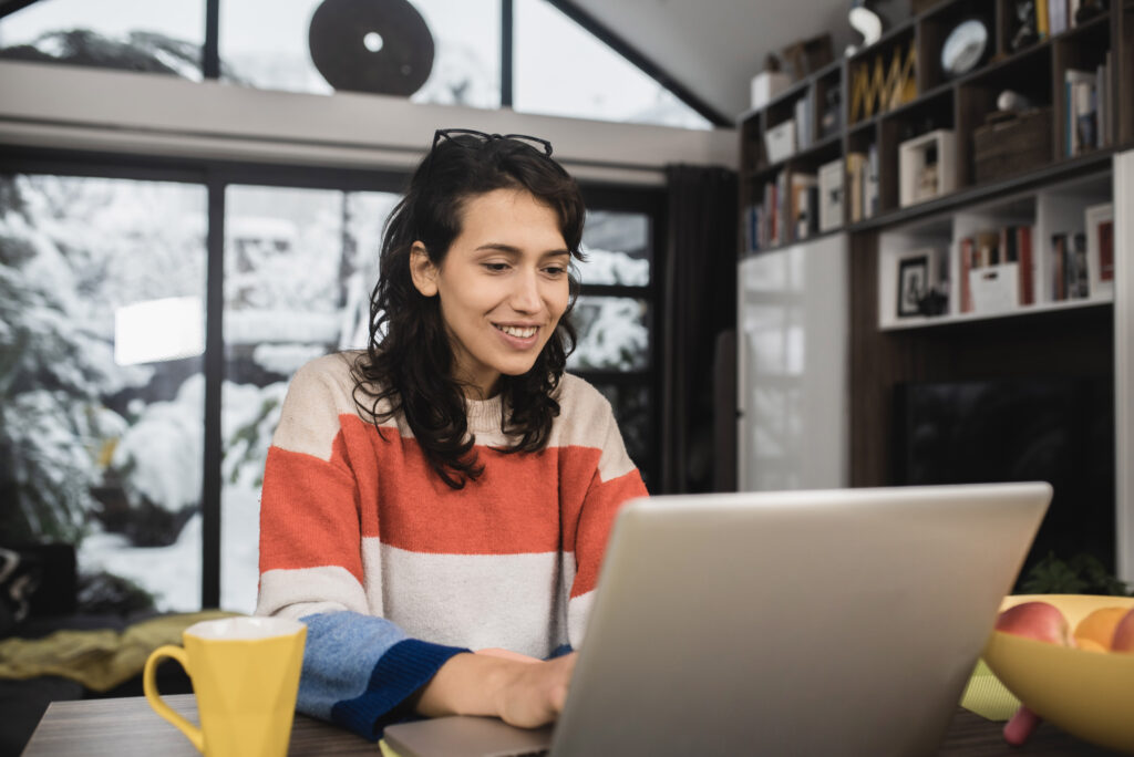 A woman in a striped sweater typing on a laptop in an apartment