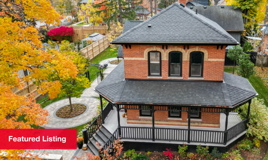 A two-storey red brick home with a wraparound porch in the fall