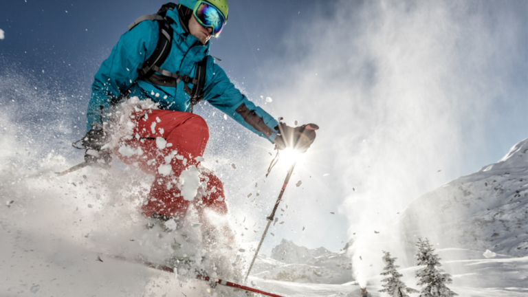 Close up of man in a blue winter parka and red snow pants skiing downhill during the day