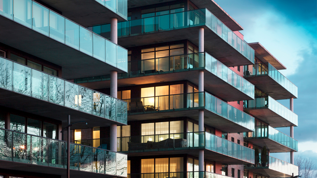 A modern mid-rise condominium building with wraparound glass balconies under dark cloudy skies