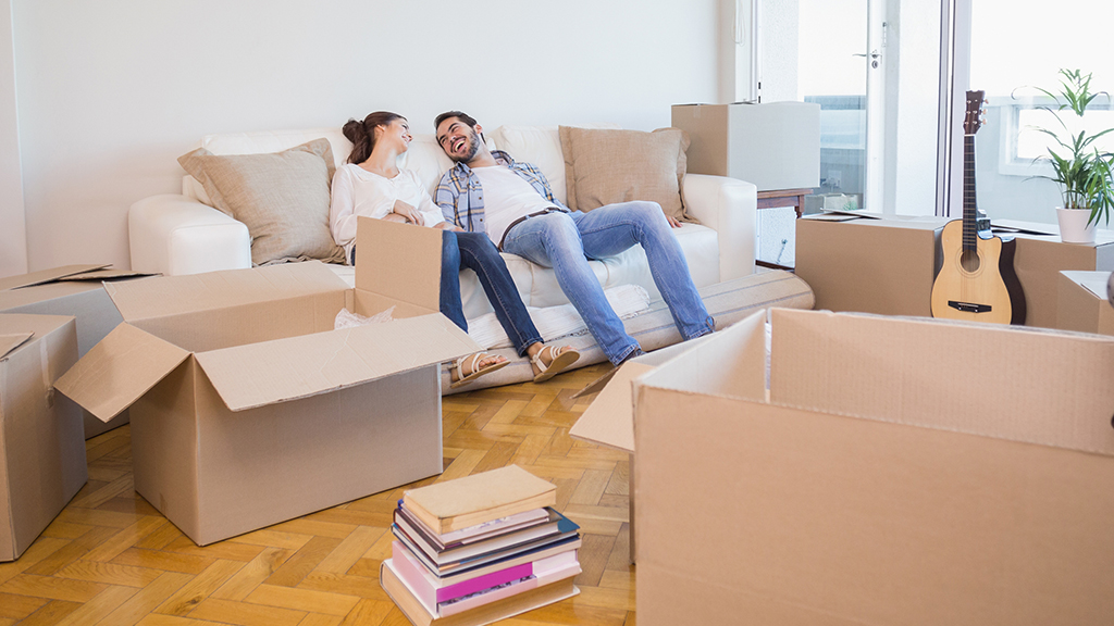 A young couple sitting on a sofa in a modern apartment surrounded by moving boxes