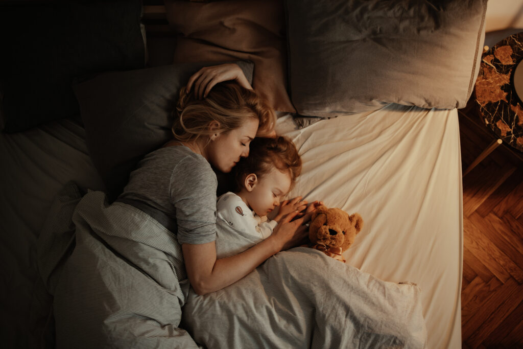 Mother and daughter sleeping together in bed with teddy bear