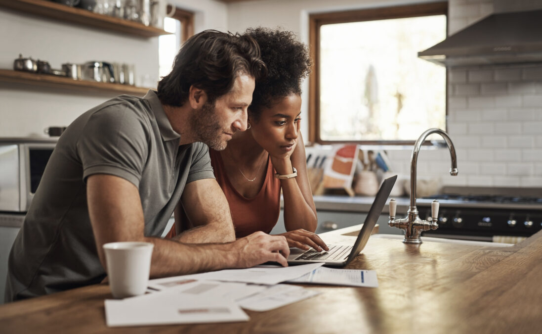 A couple using their laptop and going through paperwork on their kitchen island