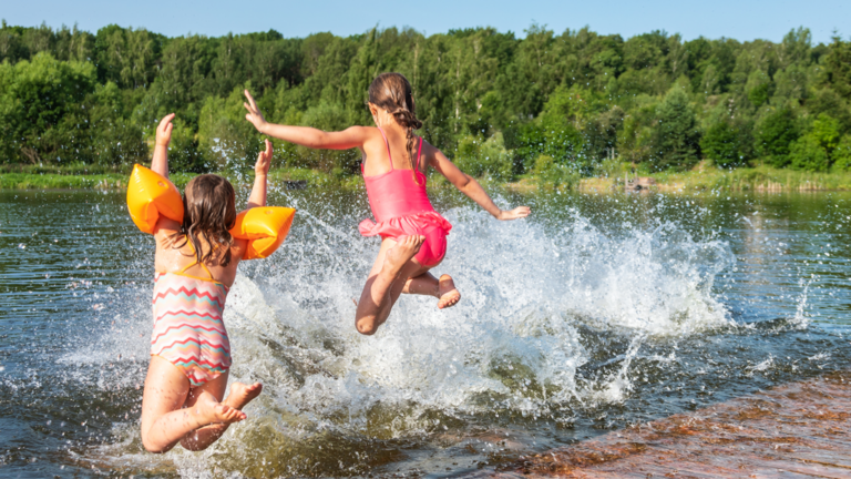 Two children in bathing suits jump off of a dock into the lake in the summertime
