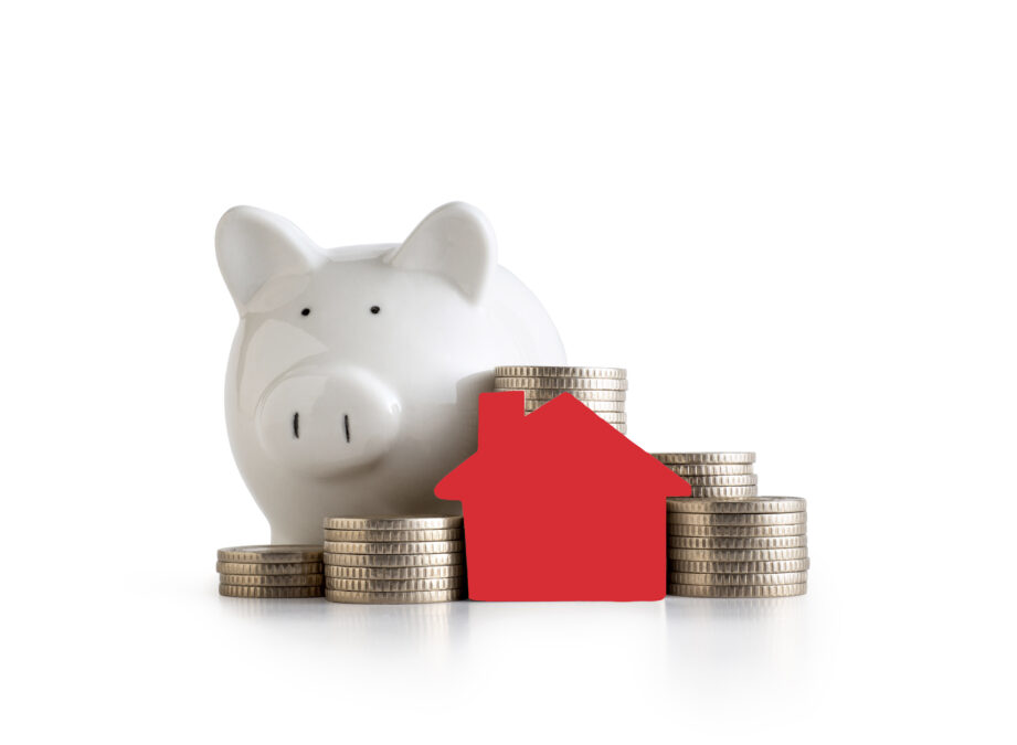 A white piggy bank next to a stack of coins and a red house