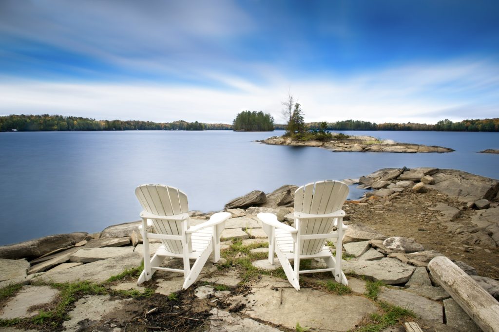 Two white Muskoka chairs sitting on rocks overlooking water