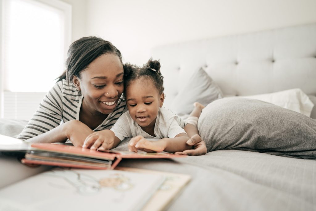 A woman and her young child read together on a bed