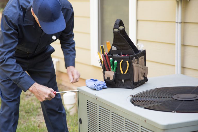 A repair technician in a blue uniform screws a panel on an HVAC unit
