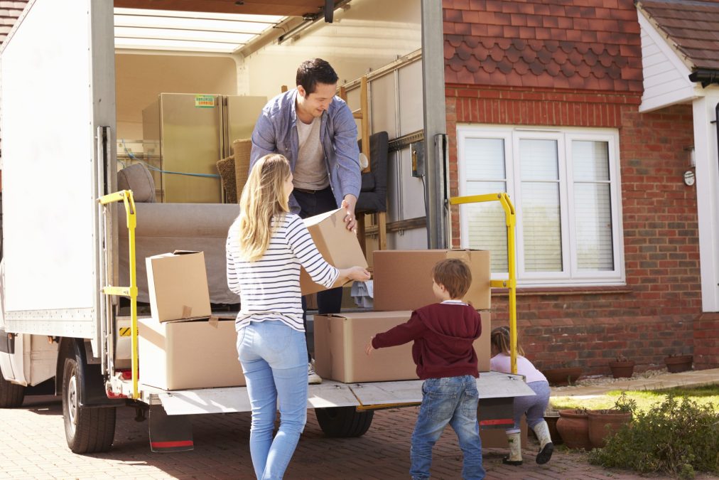A young family with children unload boxes from a moving truck to their new home