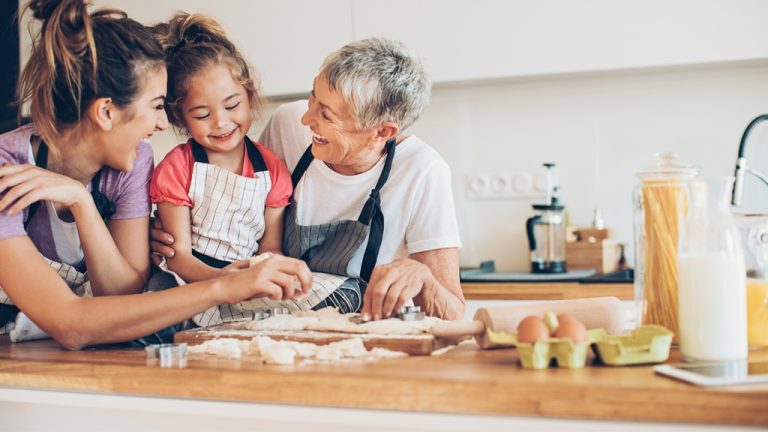 A grandmother, mother and daughter bake together in a kitchen