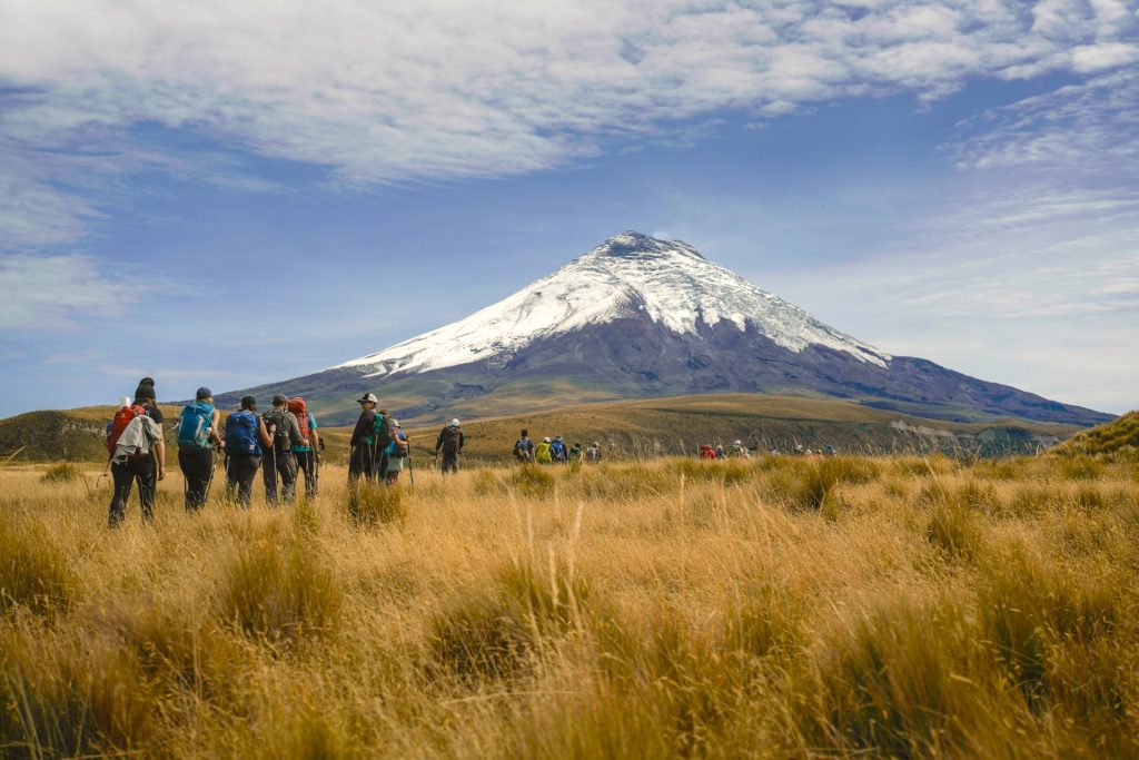 Hikers walking through field at base of Ecuadorian mountain during the day