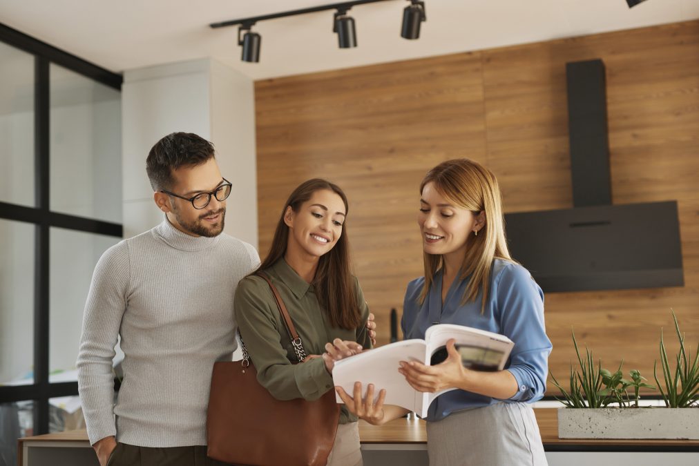Realtor and young couple flipping through booklet in modern kitchen