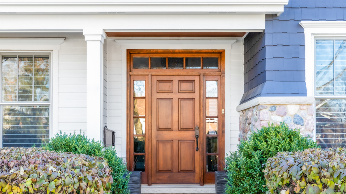 A wooden door of a single-family home with blue shingles during the day