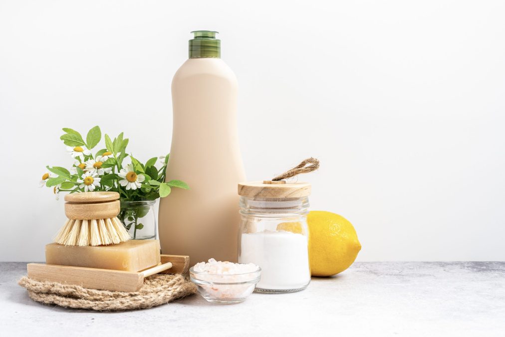 Eco friendly natural cleaners, jar with baking soda, dish brush, lemon, flowers, soap on white background