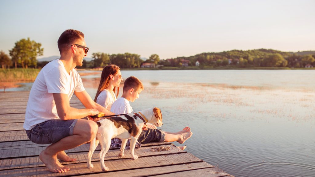 Family and dog sitting on a dock by the lake during sunset