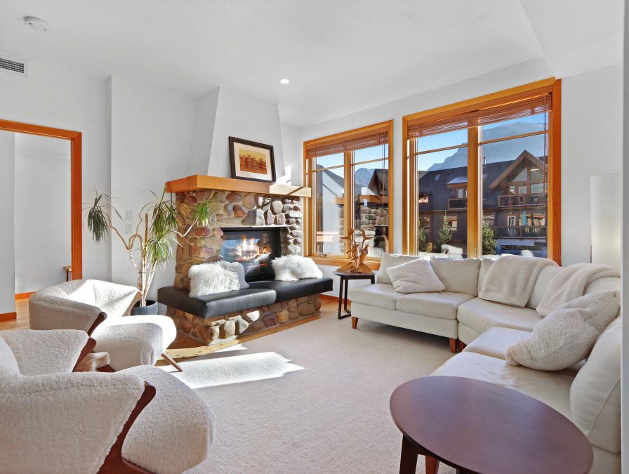 A sunlit apartment living room with a stone fireplace overlooking the Rocky Mountains