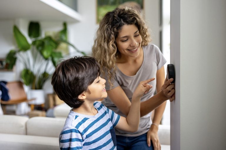Happy mother and son at home using a smart thermostat to adjust the temperature