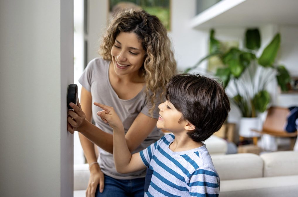 Happy mother and son at home using a smart thermostat to adjust the temperature
