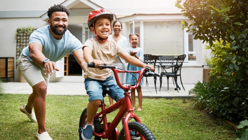 Father teaching young son to ride bicycle in backyard