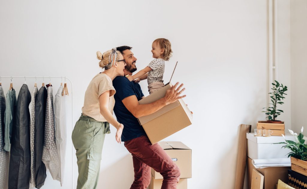 Happy family with one child having fun while carrying and unpacking boxes in new home on moving day