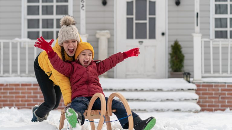 A young brother and sister in parkas playing in the snow during the day