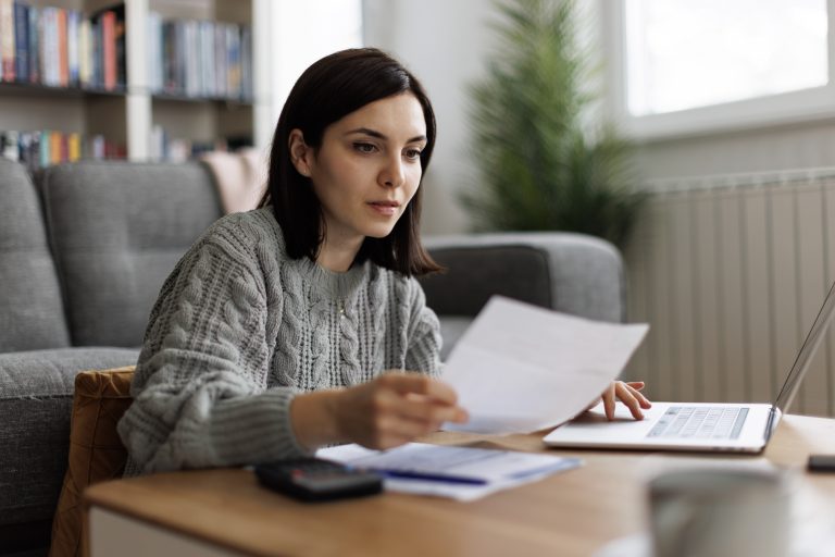 A woman in a grey sweater reading financial papers on a coffee table