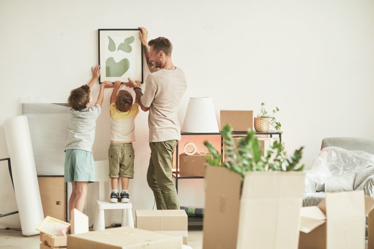 Dad and his two young sons hang a framed picture on a wall