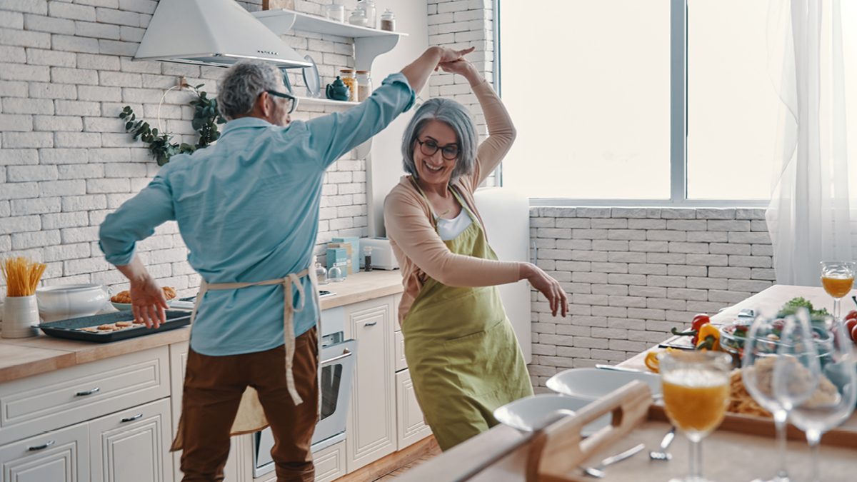 A retired couple dancing together in the kitchen