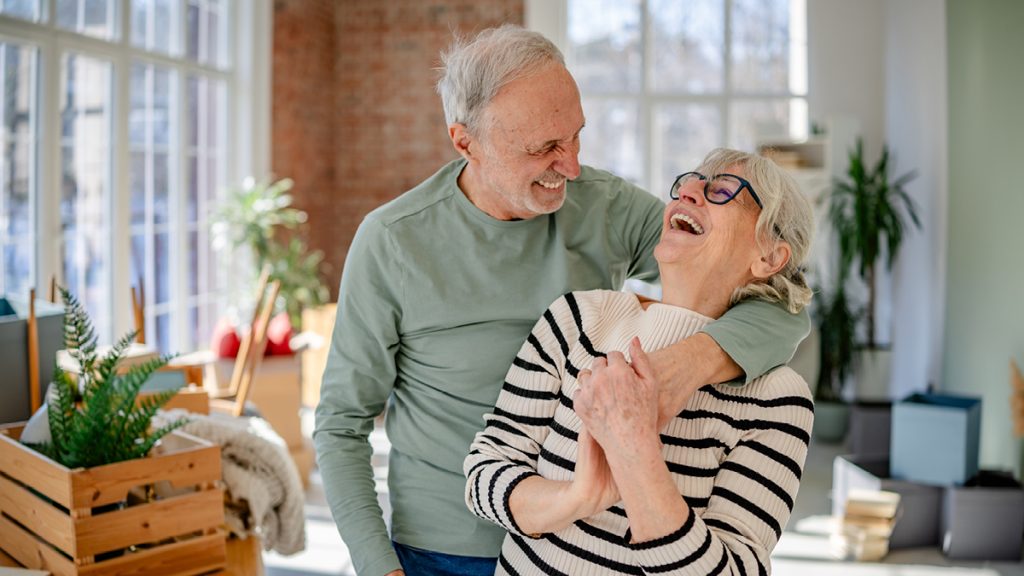 An older couple laugh together in their new home