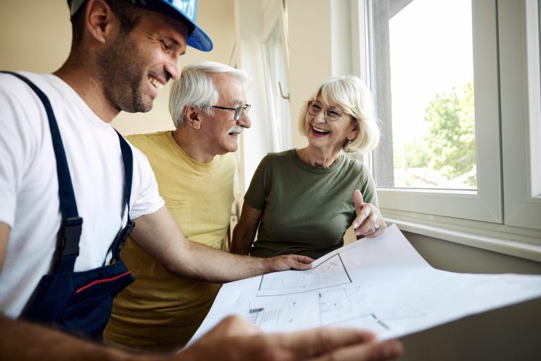 Happy mature couple examining blueprints with worker during home renovation