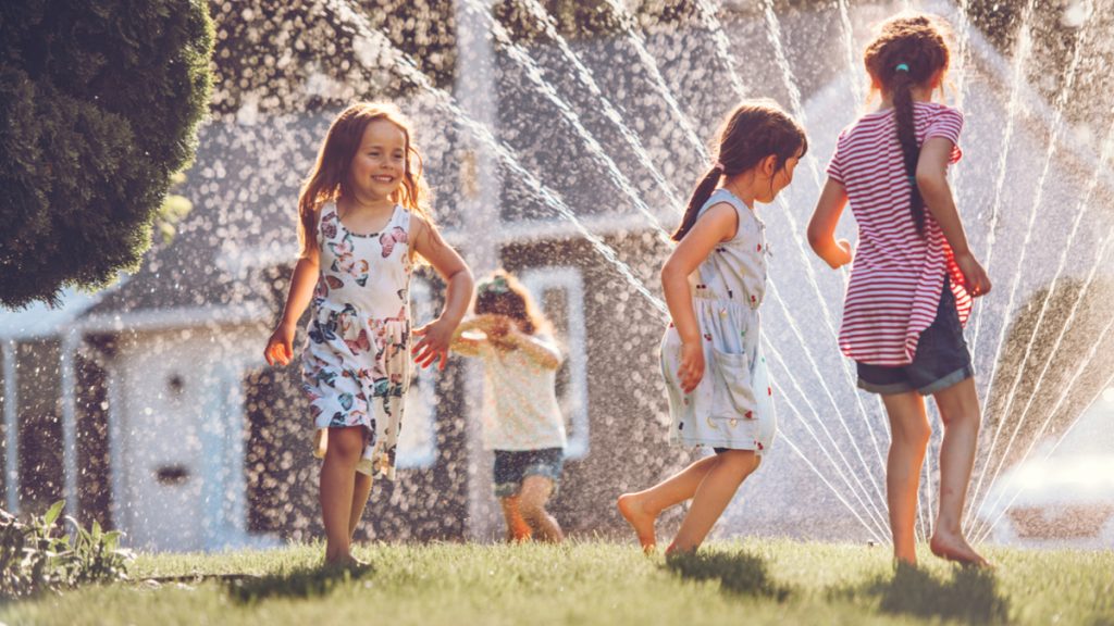 Young girls playing through a sprinkler during the day