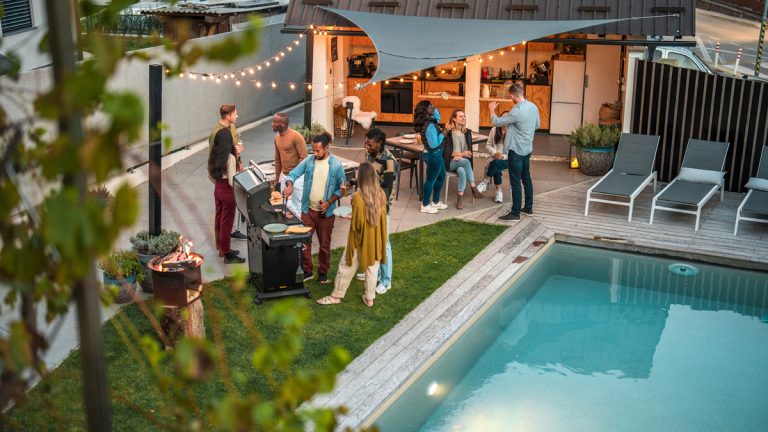 Adults gather in a backyard in the evening for a barbeque dinner